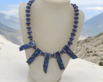 May include: A blue and silver necklace with a geometric design. The necklace features five long, rectangular blue stones with a marbled pattern and silver beads.