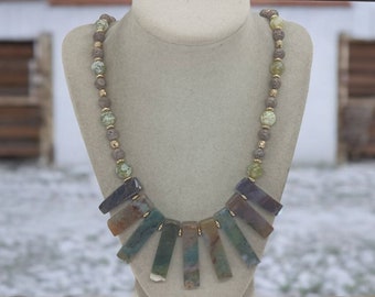 May include: A multi-colored agate stone necklace with a gold and brown beaded chain. The necklace features a fan-shaped pendant of seven agate stones in shades of green, brown, and purple.