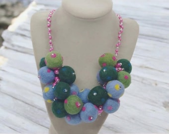 May include: A colorful felt necklace with blue, green, and pink polka dots. The necklace is made of felt balls strung together with pink beads.