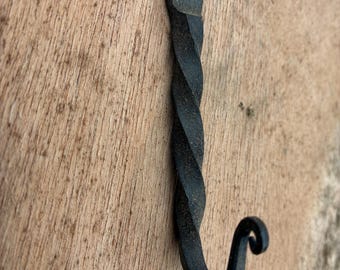 May include: A black, hand-forged metal hook with a twisted shaft and a curled end. The hook has two mounting holes at the top for easy installation. The hook is designed for hanging items.