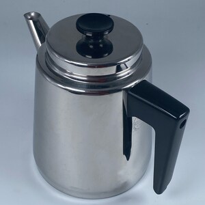 Puede incluir: Una tetera de acero inoxidable con un asa y una tapa de plástico negro. La tapa tiene un pomo negro.
