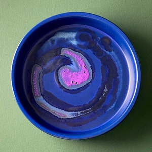 Op de afbeelding: Een blauwe harsbak met een draaiend ontwerp in tinten blauw, wit en roze. Het ontwerp heeft een centrale roze swirl met witte en blauwe accenten.