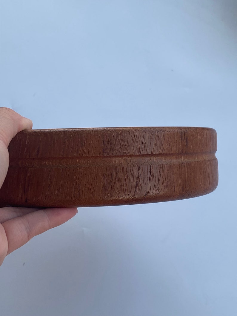 May include: A round, wooden bowl in a rich brown hue. The bowl features a smooth, polished surface and a simple, elegant design. The bowl is held by a hand against a white backdrop.