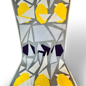 May include: A white fabric with a geometric pattern of gray, yellow, and purple triangles and squares.