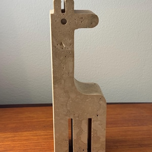 May include: A beige travertine stone sculpture of a giraffe. The sculpture is abstract and minimalist, with a simple, geometric design.