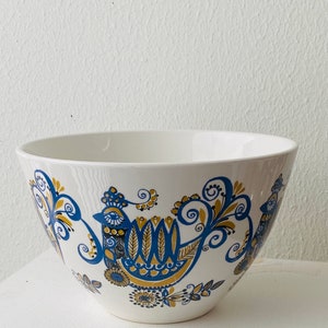 Könnte beinhalten: Eine weiße Keramikschüssel mit einem blauen und goldenen Blumenmuster. Die Schüssel zeigt ein stilisiertes Vogeldesign mit filigranen Details.