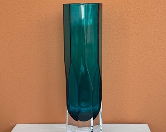Könnte beinhalten: Eine hohe, teal-farbene Glasvase mit geometrischem Design. Die Vase hat eine rechteckige Form mit facettiertem Boden und leicht ausgestelltem oberen Rand. Die Farbe Teal ist reich und lebendig, und das Glas scheint dick und hochwertig zu sein.
