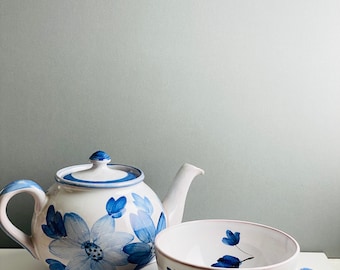 May include: A white teapot and teacup with a blue floral design. The teapot has a lid and a spout. The teacup has a handle and a saucer.