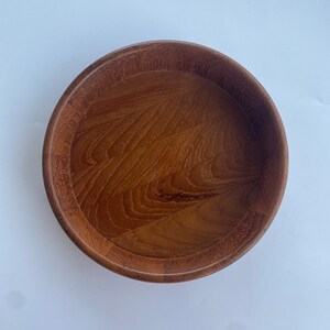 May include: A circular wooden bowl in a warm brown hue. The bowl features a raised edge and a polished interior, showcasing the wood grain. This bowl is suitable for serving food or as a decorative item. The diameter is approximately 25 cm.
