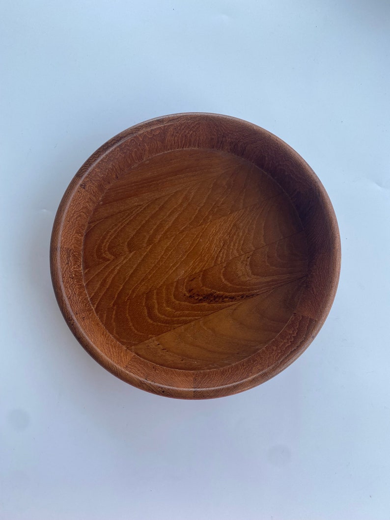 May include: A circular wooden bowl in a warm brown hue. The bowl features a raised edge and a polished interior, showcasing the wood grain. This bowl is suitable for serving food or as a decorative item. The diameter is approximately 25 cm.