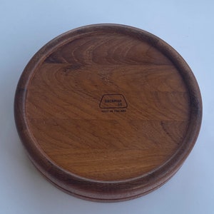 May include: A circular wooden tray with a raised rim, in a warm brown hue. The wood grain is clearly visible. The text "BACKMAN -89- MADE IN FINLAND" is stamped on the tray, indicating its origin.