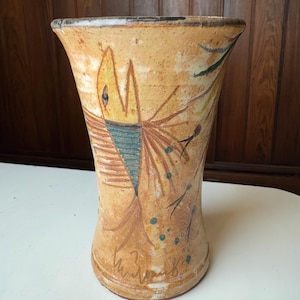 May include: A ceramic vase with a yellow, brown, and blue fish design. The vase has a flared opening and a rounded base.