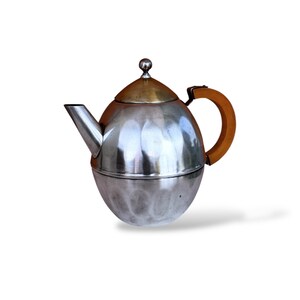 Puede incluir: Tetera plateada con cuerpo redondeado y tapa dorada. Cuenta con un asa de madera y un pico vertedor. La tetera tiene un diseño clásico, ideal para servir té.