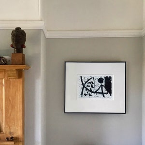 May include: A black and white abstract art print in a black frame hangs on a light gray wall. The print features black lines and shapes on a white background.