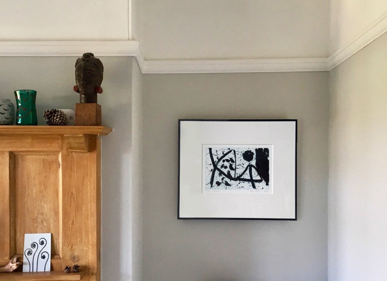 May include: A black and white abstract art print in a black frame hangs on a light gray wall. The print features black lines and shapes on a white background.