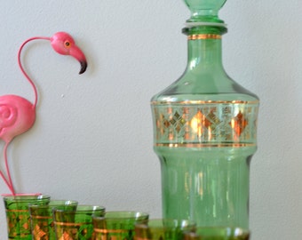 Puede incluir: Un juego de vasos de chupito de vidrio verde con detalles dorados y una jarra de vidrio verde a juego con un tapón dorado. Los vasos y la jarra tienen un patrón de diamante.