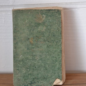 May include: A vintage green book with a worn cover and gold lettering. The book is sitting on a wooden surface.