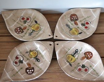 May include: Set of four leaf-shaped ceramic serving dishes with a brown rim. Each dish features a different design of a mushroom, onion, and apple in shades of red, yellow, brown, and white on a beige background.