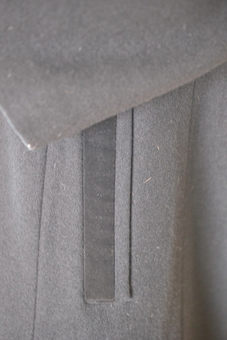 May include: Close-up of a black fabric with a vertical seam and a black fabric pocket.