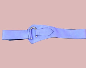 May include: A light purple belt with a silver-colored buckle. The belt is wide and has a pointed end. The buckle is a simple, curved design. The belt is made of a smooth material.