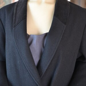 May include: A black wool blazer with a wide collar and gold buttons. The blazer has a single breasted closure and a long, fitted silhouette.