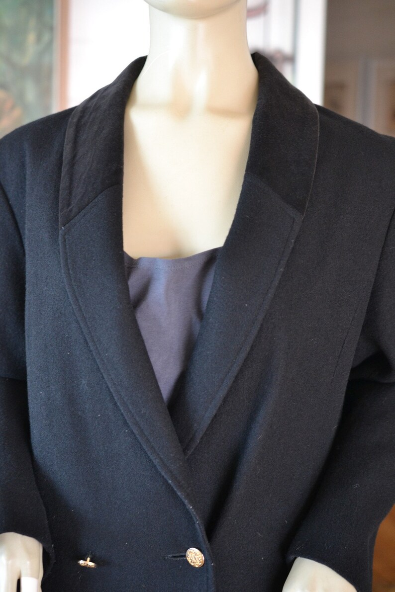 May include: A black wool blazer with a wide collar and gold buttons. The blazer has a single breasted closure and a long, fitted silhouette.