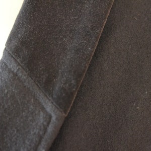 May include: Close-up of a dark gray fabric with a textured surface. The fabric is folded over, showing the inside of the fold.