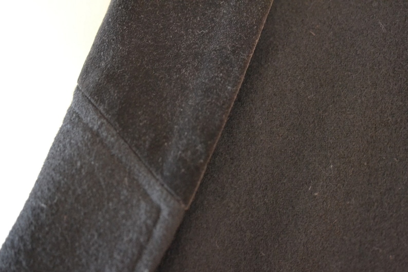 May include: Close-up of a dark gray fabric with a textured surface. The fabric is folded over, showing the inside of the fold.