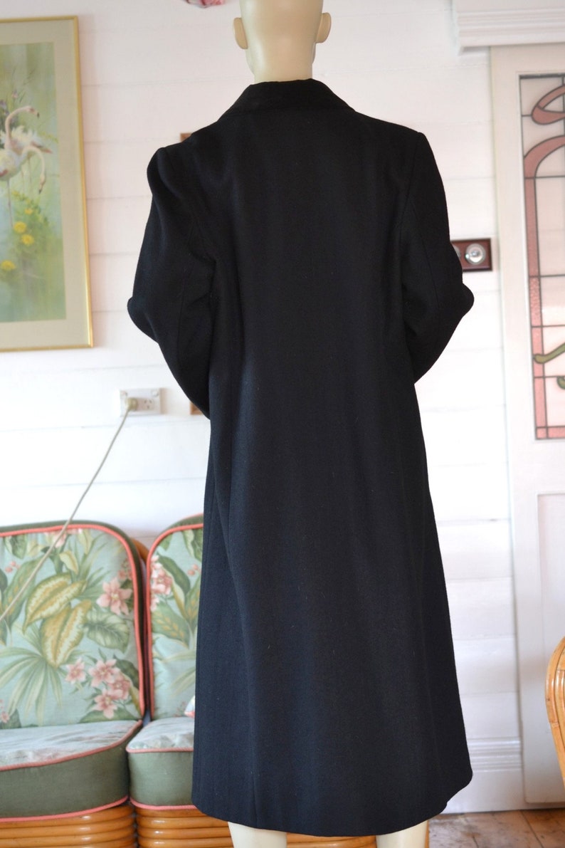 May include: A long black coat with a collar and long sleeves. The coat is made of a smooth fabric and has a simple design.