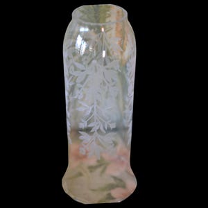Könnte beinhalten: Eine klare Glasvase mit ausgestelltem Boden und leicht breiterem oberen Rand. Die Vase ist mit einem zarten floralen Muster aus Blättern und Blüten geätzt. Das Glas hat einen leichten Gelbstich.