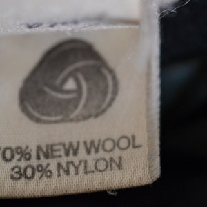 May include: A white fabric label with a gray swirl design and the text "70% NEW WOOL 30% NYLON".