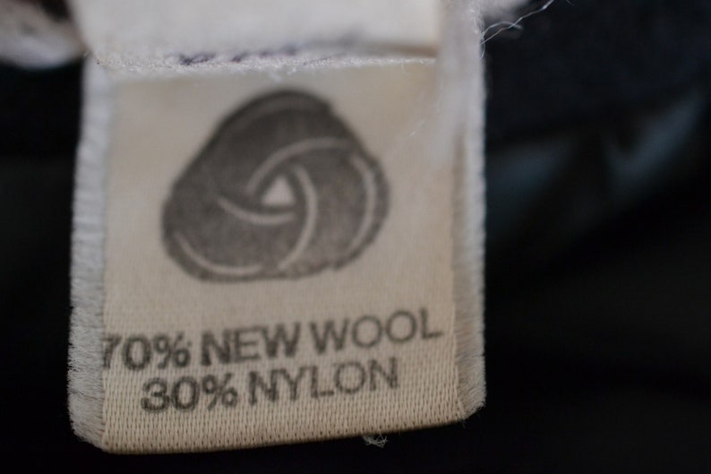May include: A white fabric label with a gray swirl design and the text "70% NEW WOOL 30% NYLON".