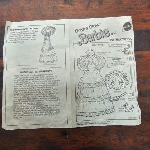 Könnte beinhalten: Ein Anleitungsblatt für eine Vintage-Barbie-Puppe. Das Blatt enthält Illustrationen der Puppe, des Zubehörs und Anweisungen für die "Dream Glow"-Funktion. Es enthält auch eine 90-Tage-Garantie und Kontaktinformationen.
