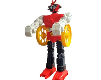 Puede incluir: Un juguete de robot vintage en rojo, blanco, negro y amarillo. El robot tiene un torso y una cabeza rojos, brazos blancos, piernas negras y ruedas amarillas. El juguete está de pie con los brazos doblados.