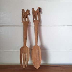 May include: A set of two wooden serving utensils with monkey carvings on the handles. The utensils are a fork and a spoon.