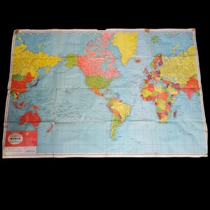 May include: A folded vintage world map, featuring countries in a variety of colours, including red, yellow, green, and blue. The ocean is light blue. A red and white label is in the lower left corner. The map is set against a black background.