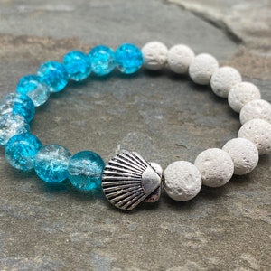 May include: A blue and white beaded bracelet with a silver seashell charm. The bracelet is made with small, round beads and has a gradient color scheme, transitioning from blue to white.