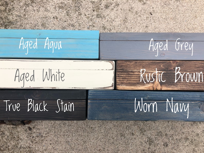 May include: A collection of stained wood samples in various colors, including Aged Aqua, Aged Grey, Aged White, Rustic Brown, True Black Stain, and Worn Navy. Each sample has the color name written in white script.