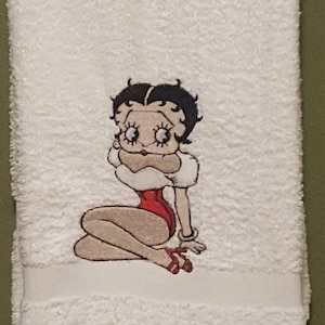 Puede incluir: Toalla de baño blanca con una imagen bordada de una mujer de dibujos animados con cabello negro, labios rojos y un vestido rojo.