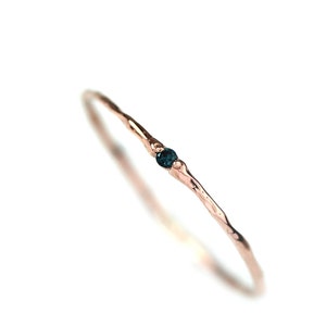 Op de afbeelding: Een delicate roségouden ring met een getextureerde band en een kleine, donkerblauwe edelsteen. De ring staat tegen een effen witte achtergrond, wat de eenvoudige elegantie en fijne afwerking benadrukt.