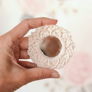 May include: A white crocheted mirror with a round frame. The mirror is small and would be perfect for a vanity or dresser.