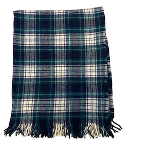 May include: A rectangular woven throw blanket featuring a dark green, navy blue, and off-white plaid pattern. The fabric has a soft, textured appearance with visible horizontal and vertical lines forming squares, finished with a fringed edge.