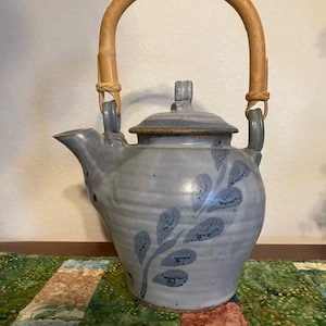May include: A blue ceramic teapot with a bamboo handle and a leaf design. The teapot has a lid and a spout.