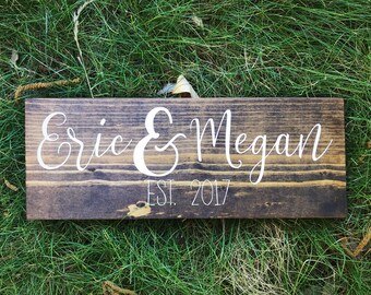 May include: A rustic wooden sign with the names "Eric & Megan" and the text "EST. 2017" in white lettering.