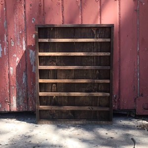 May include: A dark brown wooden shelf with six shelves. The shelf is standing in front of a red wooden wall.