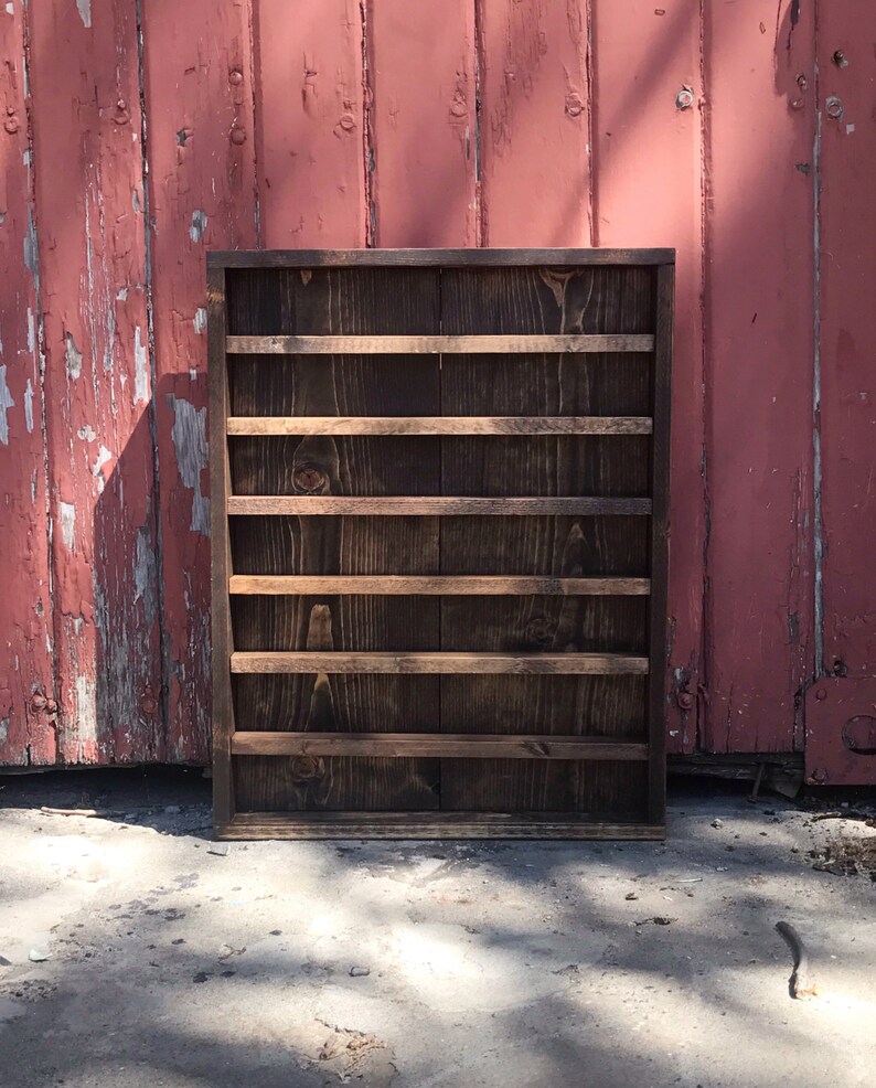 May include: A dark brown wooden shelf with six shelves. The shelf is standing in front of a red wooden wall.
