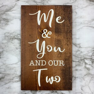 May include: A wooden sign with the text "Me & You And Our Two" in white paint. The sign has a rustic brown finish.
