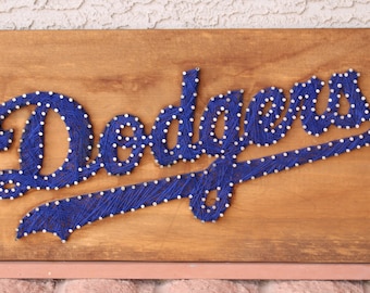 May include: A wooden sign with the word "Dodgers" spelled out in blue string wrapped around nails. The nails are evenly spaced and create a clean, professional look.