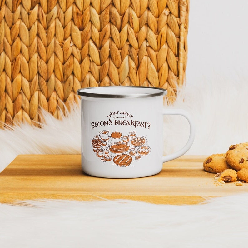 May include: White enamel camping mug with a brown outline and text that reads "What about Second Breakfast?"  The mug features a drawing of a variety of breakfast foods, including bread, eggs, and fruit.