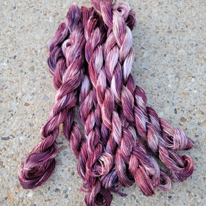 K&ouml;nnte beinhalten: Ein B&uuml;ndel mit sechs Kn&auml;uel Stickgarn in den Farben Burgunderrot, Rosa und Wei&szlig;. Das Garn ist gedreht und hat ein mehrfarbiges Muster.